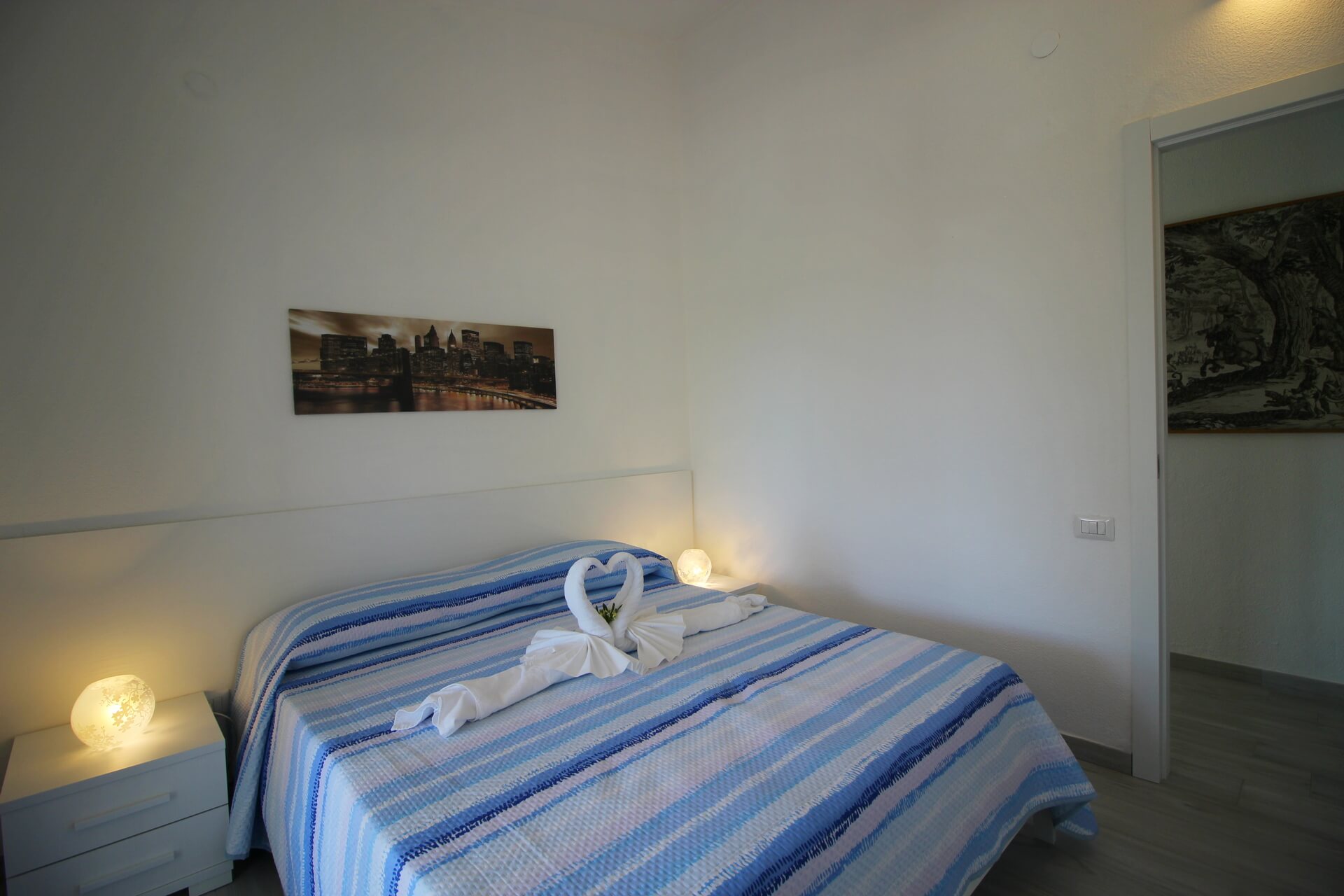 Letto matrimoniale con lenzuola a righe blu e bianche, lampade da comodino accese